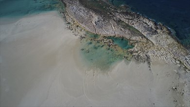 Drone shot, coastline with wide sandy beach and clear blue water, interspersed with rocks,