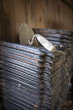 Many roof tiles stacked in a barn, on top an old spatula, cobwebs, background wooden wall,