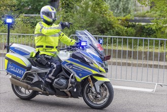 A policeman in a high-visibility waistcoat rides a police motorbike with blue lights and shows the