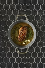 Top view of a perfectly seared duck breast with fresh thyme and garlic in a cooking pan