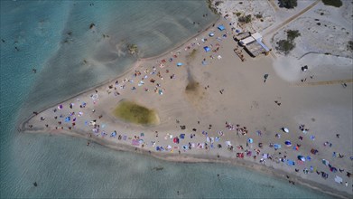 Overtourism, aerial view of a beach with many people and colourful umbrellas enjoying the sand and