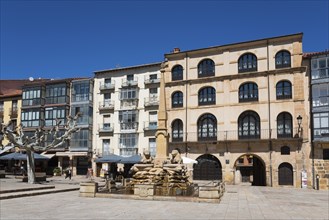 A quiet square with a fountain in the centre, surrounded by historic buildings under a clear blue