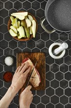 A chef skillfully slices criss-cross a juicy piece of duck breast fat on a rustic wooden cutting