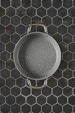 Top view of double handled non-stick frying pan on hexagon tile background