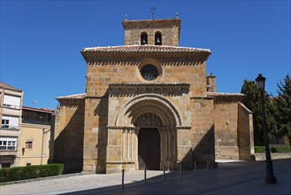 Romanesque church with stone façade and tower under a clear blue sky, surrounded by buildings,