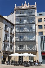 A modern building with balconies and an outdoor café, including tables and chairs under a clear