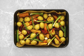 Overhead view of baking tray with fresh vegetables and spices on kitchen countertop