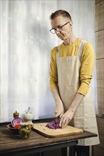 Middle-aged man chopping red cabbage in the kitchen