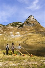 Three men play the alphorn at Lake Augstsee on Mount Loser. The Austrian alphorn trio Klangholz.