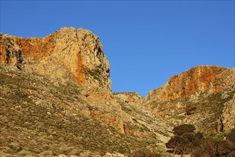 Morning light, natural landscape with sunlit rocks and hills under a cloudless blue sky, Gramvoussa