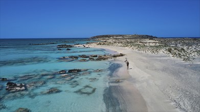 A person walks on the sandy, rocky shore along the clear blue sea. Quiet and unspoilt nature,