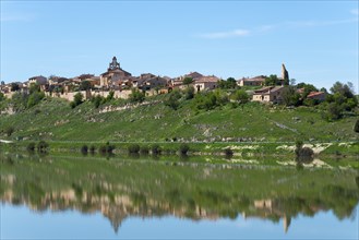 A picturesque village on a hill is reflected in a calm lake under a clear blue sky, Maderuelo, Río