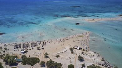 Overtourism, aerial view of a beach with people and umbrellas surrounded by blue sea water,