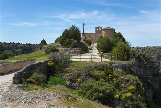 A small historic church with a stone cross on a hill surrounded by trees and a path in a peaceful