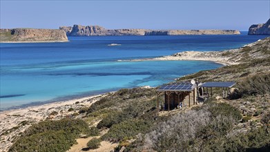 Caretaker building, coastal landscape with blue water, solar panels and green hills, quiet beach,