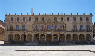 A large historic building with arcades and flags stretching across a spacious square under a blue