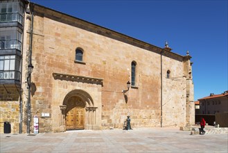 A simple historic church with a sandstone-coloured façade and large doors in an empty square under