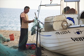 Fisherman in Armacao de Pera, Algarve, Portugal, fisherman preparing a net next to a boat on the