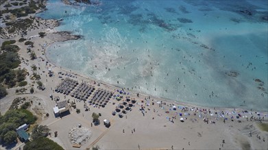 Overtourism, aerial view of a beach with many people and umbrellas, surrounded by clear water,