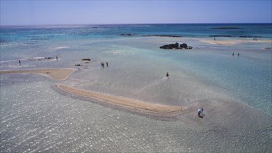 Sandbank in clear, calm sea with scattered people enjoying the natural surroundings, Elafonissi,