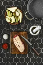 Overhead view of raw duck breast with the skin cut crosswise on wooden chopping board surrounded