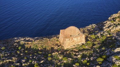 Drone shot, A single ruin on a rocky cliff above the blue sea, surrounded by vegetation, square