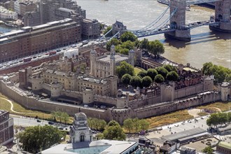 Historic Tower of London castle on the riverside, surrounded by modern buildings and Tower Bridge,