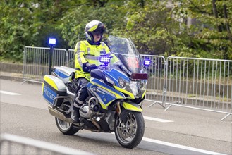 A police officer rides a motorbike with blue lights during an operation, surrounded by barriers on