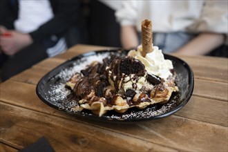 Belgian waffle with vanilla ice cream and whipped cream, waffle rolls, chocolate sauce and Oreo