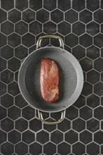 Top view of a raw duck breast lying on a non-stick pan with two handles, against a background of