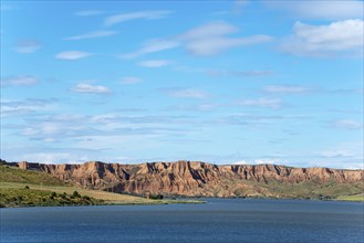 A clear blue lake surrounded by majestic rock formations and rolling hills under an expansive sky,