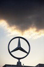 Symbolic image, Dark clouds at Mercedes, Mercedes-Benz logo in front of a sunset sky with clouds