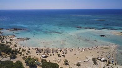 Overtourism, sandy beach with many parasols and people enjoying the clear blue sea. The sky is