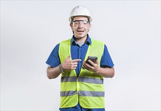 Smiling engineer holding phone and looking at camera isolated. Latin male builder engineer using