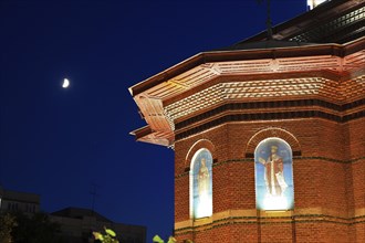 An illuminated church with brick façade and stained glass windows at night under a clear night sky