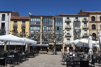 A lively square with tables and chairs in front of cafés and colourful buildings under a clear blue