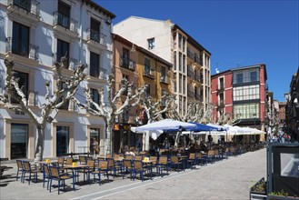 An empty sidewalk café along a row of buildings in clear, sunny weather with blue umbrellas and