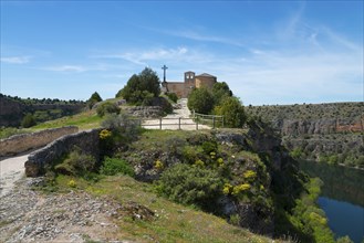 A picturesque church stands on a lush hill with a path, under a bright blue sky in a vast