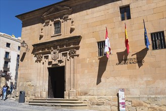 A historic building with flags and a large entrance with a few people in front of it, under a clear