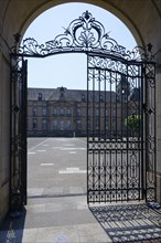 Iron gate opens onto a sunny courtyard with historic building, Echternach Abbey, Echternach,