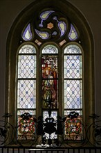 Interior view, Gothic church window with richly decorated stained glass and a figure of a saint in