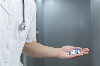 Close up of male doctor in uniform with stethoscope and holding blue and white pills in a hand