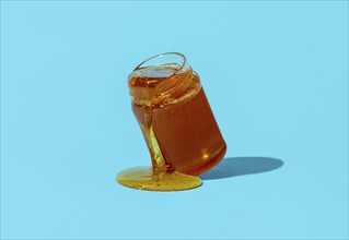 Jar with honey minimalist on a blue table. Dripping honey from a glass jar directly on the table