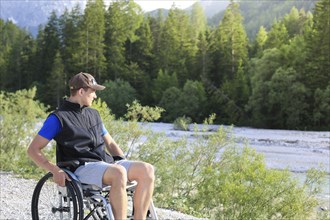 Happy young man in wheelchair outside in nature on a sunny summer day