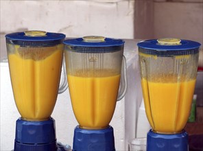 Three electric blenders are making fresh mango smoothies