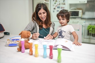 A woman and a child are sitting at a table with a book and a teddy bear