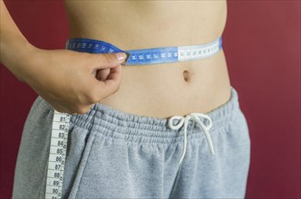 Skinny young woman measuring her slim waist with a measuring tape