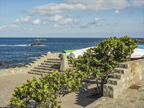 Stone steps at the edge of the ocean with boats, plants and clouds in the sky, tenerife, canary