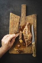 Man picking a piece of a seared dry aged rib eye steak from a wooden board