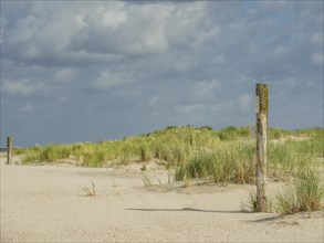 Sandy dunes with grass, cloudy sky and wooden posts, spiekeroog, east frisia, north sea, germany